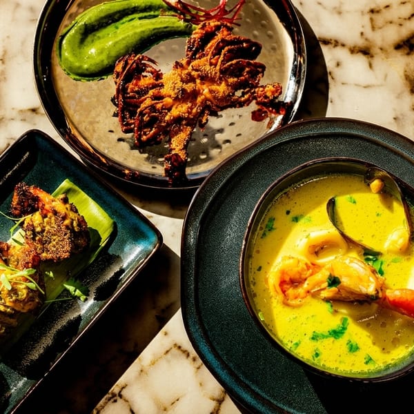 Three seafood dishes on a marble table: fried calamari, grilled shrimp, and a yellow seafood curry.