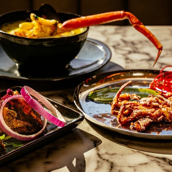 Three plates of seafood dishes, including crab legs in a bowl, fried soft-shell crab, and grilled prawns.