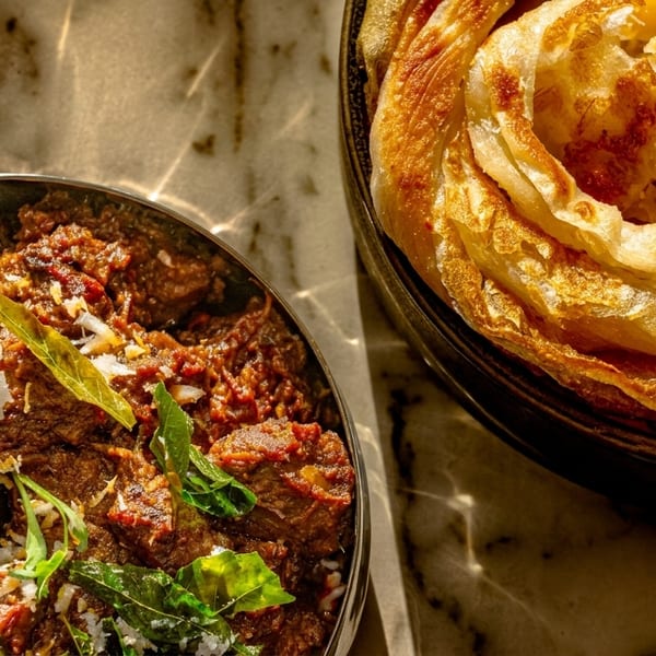 Spicy beef curry with a dried chili and fresh herbs, next to a stack of flaky paratha.